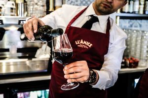 En servitör håller i en vinflaska och häller upp ett glas rött vin på Ll'Amice